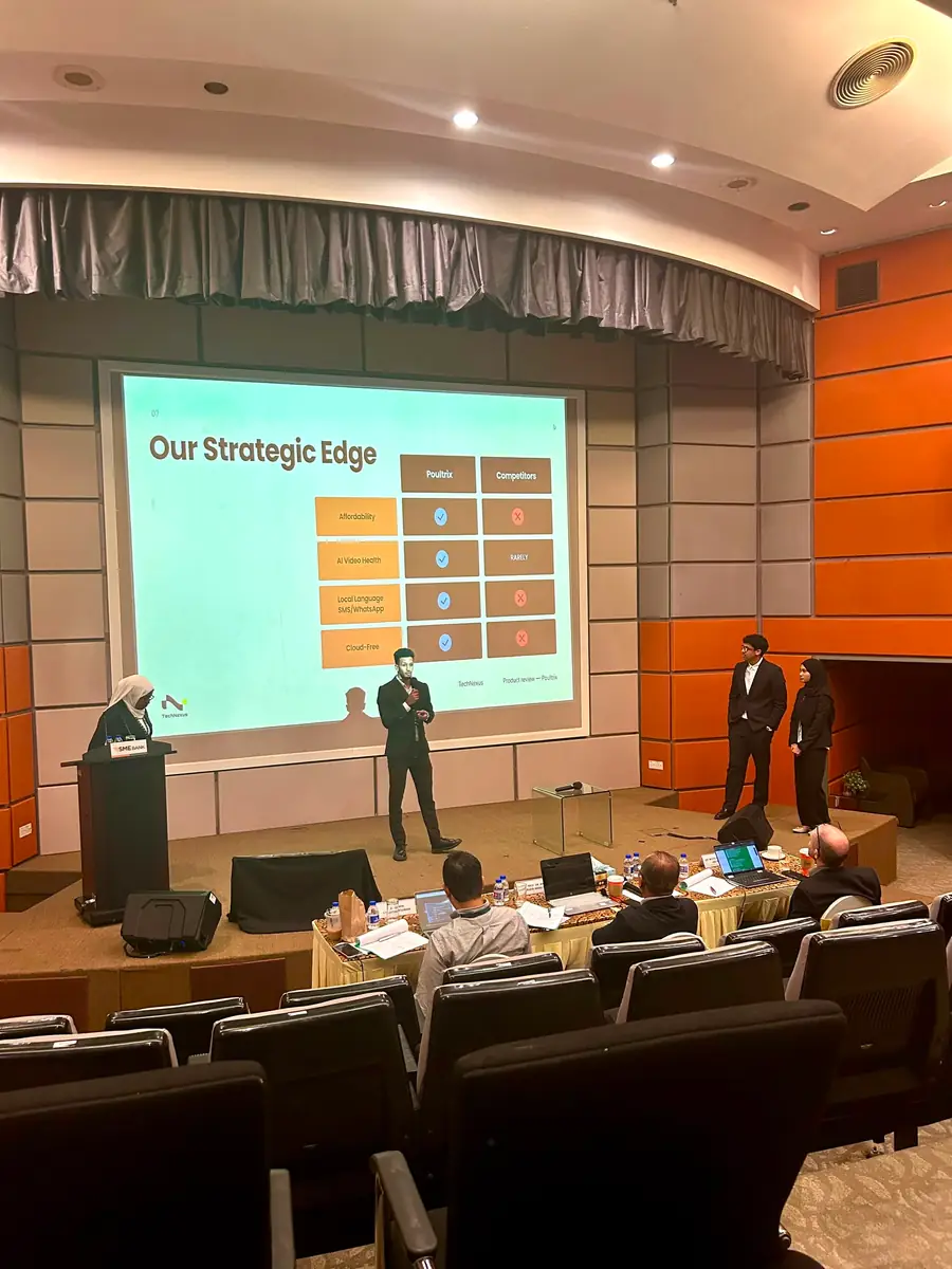 Mustafa presenting a slide titled "Our Strategic Edge" to a seated panel in a university auditorium.