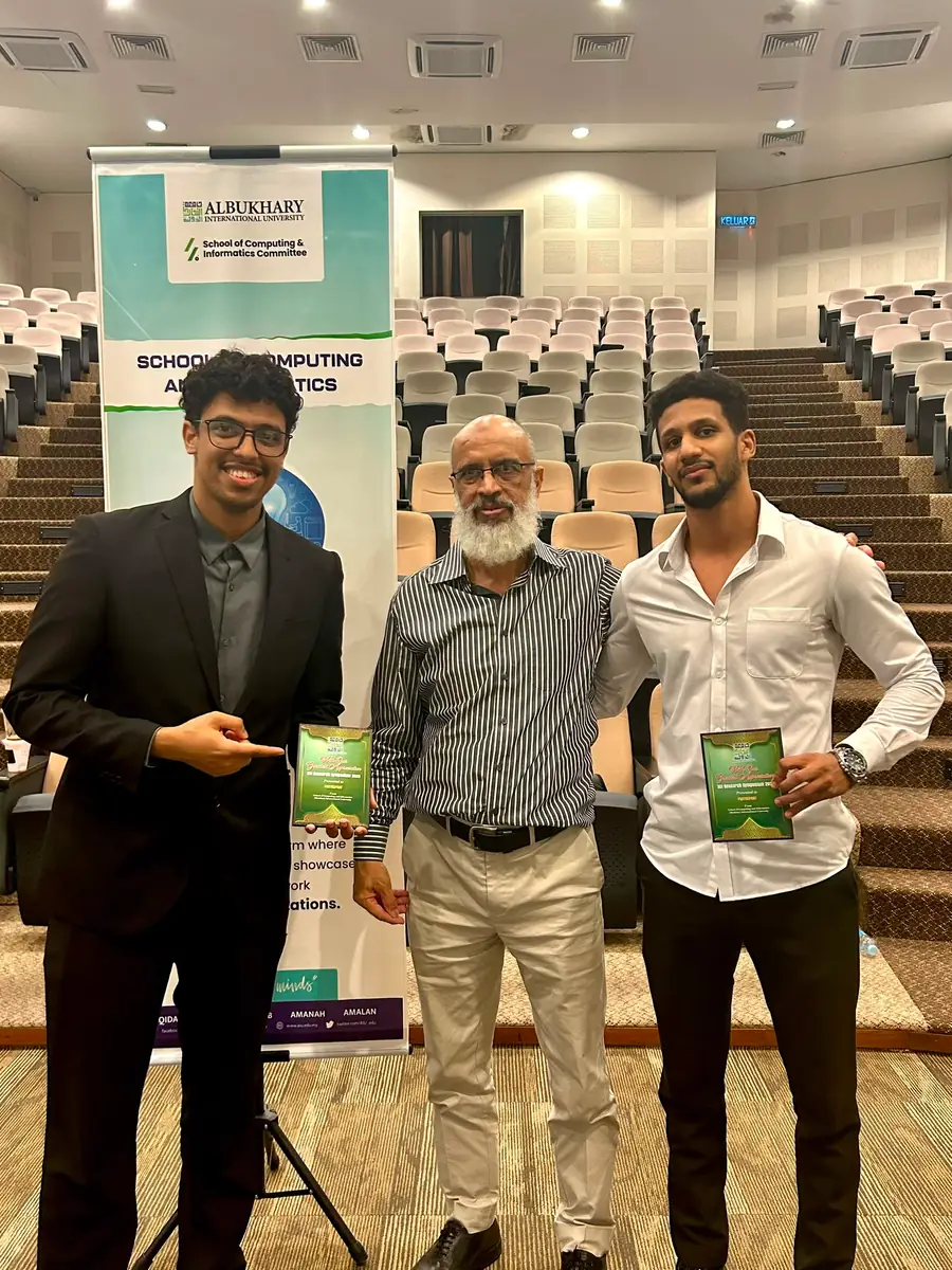 With two others in front of a School of Computing and Informatics banner.
